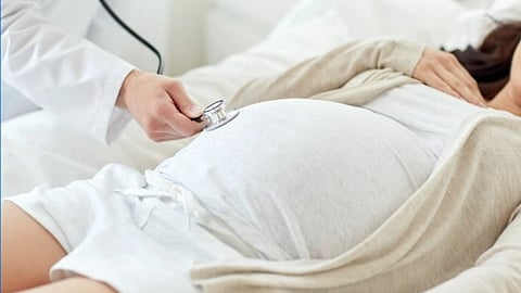 A doctor uses a stethoscope on the belly of a pregnant woman lying on a bed. The scene is calm and focused on prenatal care.