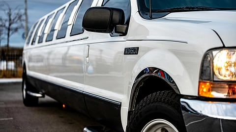 Close-up of a white stretch limousine with tinted windows on a road. Its headlights are on, emphasizing the luxurious, sophisticated vibe.