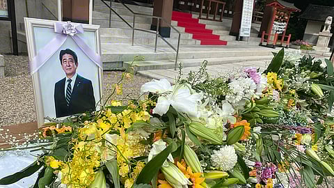 In the image a frame of Shinzo Abe is shown with flowers in front of the frame