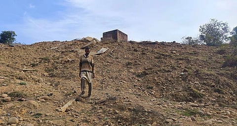 A man walks down a hill covered in upturned dirt. a small building stands at the top.