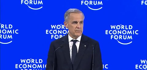 A person in a suit speaks at the World Economic Forum. The backdrop displays the event's logo repeatedly on a blue background, conveying a formal tone.