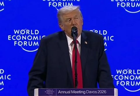 Image of US president Donald trump speaking at the Davos 2026. behind him is a blue background with the text 'world economic forum' written. 