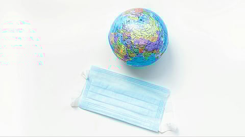 Image of a small globe positioned above a blue surgical mask on a white background, symbolizing global health and pandemic awareness.
