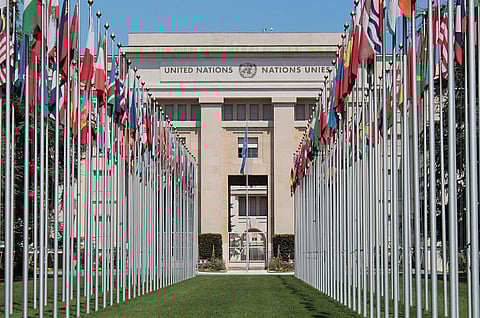 Image of  United Nations Headquarters, Geneva. A row of international flags leads to the grand facade of the United Nations building under a clear blue sky, conveying unity and diplomacy.