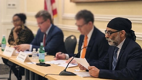 A panel discussion. Gurpatwant Singh Pannun looking at a file, sitting at a desk, along with some other people, their faces are blurrd