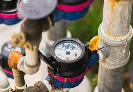 Close-up of multiple water meters in a vertical arrangement, connected by blue and red pipes. The scene conveys utility and infrastructure.