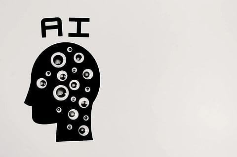 Silhouette of a head filled with various-sized googly eyes, below the letters "AI" on a light background, symbolizing artificial intelligence and awareness.