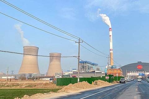 Power plant of China - 2 plants next to a chimney spewing steam in front of a road.