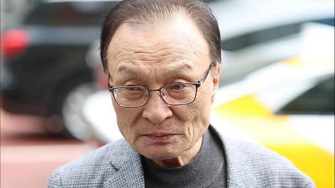 Former South Korean Prime Minister Lee Hae-chan with glasses, wearing a gray checkered jacket over a dark turtleneck, stands outdoors.