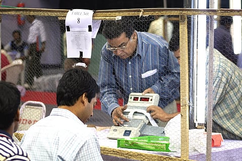 Election offciers seperated by a mesh counting votes. one is standing with an EVM while the other is sitting.
