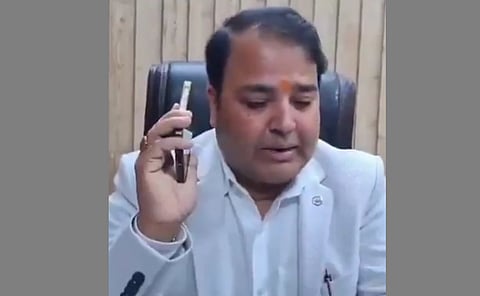 A screengrab of Prashant Singh's press conference, he is wearing a suit, sitting on a chair holding his phone 