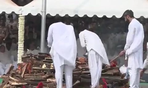 Three people dressed in white perform a Hindu cremation ceremony, placing wood on a pyre.