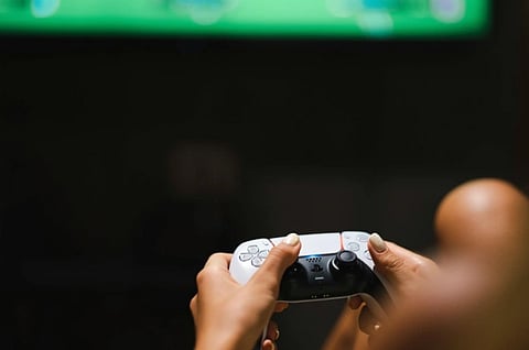 A person holding a game controller, focused on a screen with a blurred green hue. The setting is dimly lit, creating an immersive gaming atmosphere.