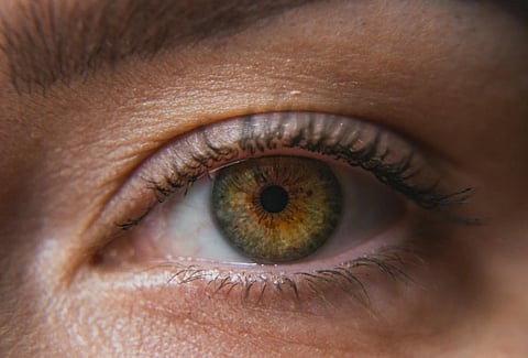 Close-up of a human eye with hazel iris, detailed textures and natural lighting. The eyelashes and eyebrow frame the eye, conveying a sense of calm focus.