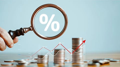 A magnifying glass focuses on a large percentage symbol above stacked coins. A fluctuating line graph with a red arrow suggests financial growth or analysis.