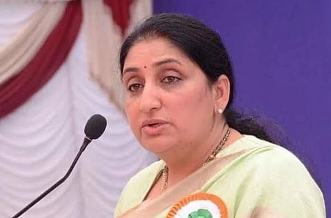 Image of Sunetra Pawar speaking at a podium with a microphone, wearing a light green saree and a ribbon on her chest. 