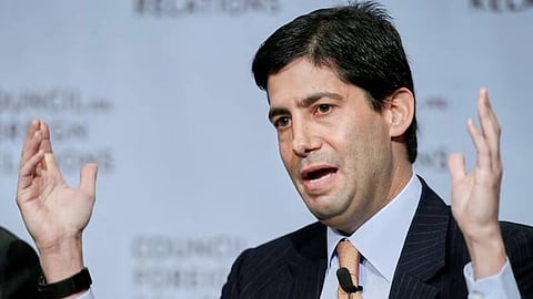 In the image Kevin Warsh is shown speaking to someone with his hands up, the setting looks formal
