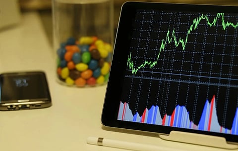 A tablet displays a rising graph, symbolizing positive financial performance. Nearby are a jar of colorful candies, a smartphone, and a stylus, conveying a dynamic and modern workspace.