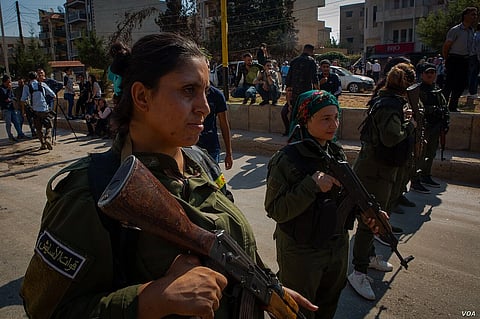 Kurdish soldiers standing in uniforms with guns in the middle of the road.