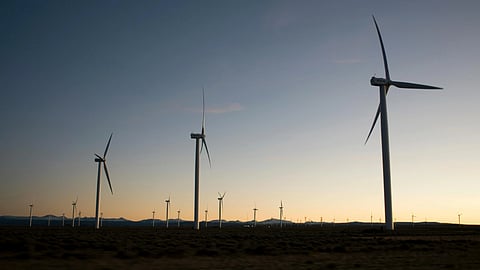 Wind turbines silhouetted against a calm sunset, scattered across a vast, flat landscape. Quiet energy is conveyed by the serene sky and expansive scene.