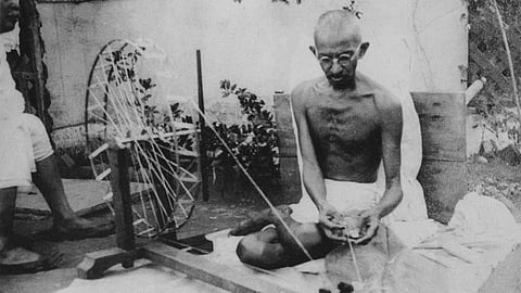 Mahatma Gandhi spinning a cotton wheel, wearing his dhoti, in a traditional home surrounding