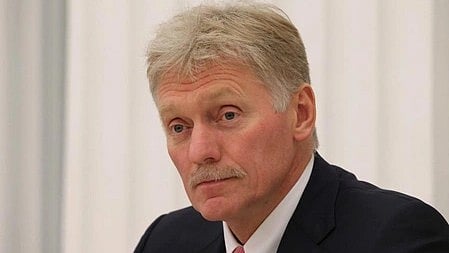 A closeup image of Russian spokesperson Dmitry Sergeyevich Peskov with gray hair and mustache, wearing a dark suit and red tie, looks thoughtful against a light, blurred background.