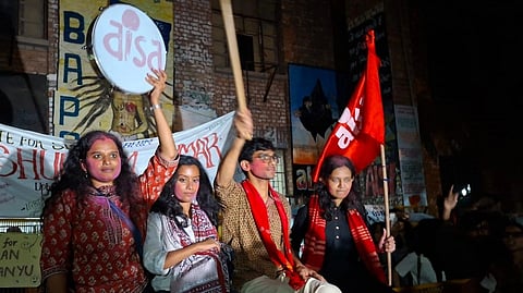 NUSU President Aditi Mishra, Vice President Gopika Babu, General Secretary Sunil Yadav, Joint Secretary Danish Ali raise flags and logos of their parties while sitting in front of banners.