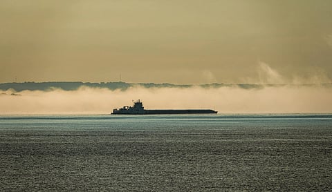 Representational image of A cargo ship sailing across a calm sea under an overcast sky. Mist shrouds the distant shoreline.