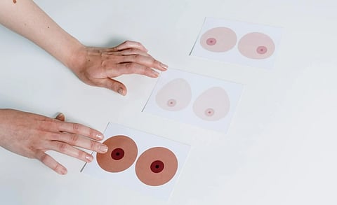 Hands arrange three cards on a white surface, each displaying different illustrations of nipples in diverse skin tones, conveying inclusivity.