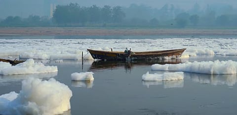 Toxic froth in the Yamuna river, a fisherman rides a boat