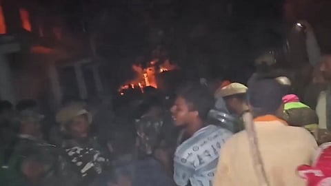 Screenshot from a video showing a mob in Dutkaiya village along with police personnel while something burns in the background.