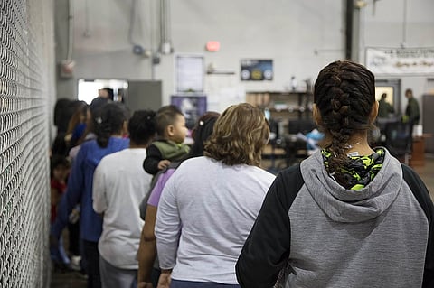 Women stand in a queue next to a fence at a detention center.