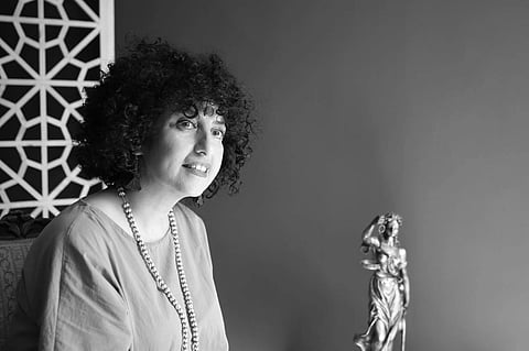 Narges Mohammadi is sitting looking to her right (slightly), there is a statue of justice beside her