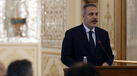 Image of Iranian and Turkish Foreign Ministers Seyyed Abbas Araghchi and Hakan Fidan meeting at the Foreign Ministry. he is speaking at a podium with a microphone in an ornate room, featuring intricate, reflective wall designs.