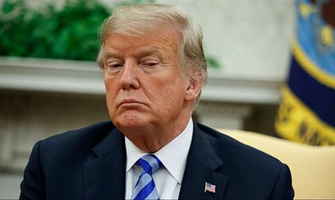 A portrait of US President Donald Trump glancing sidewards with a serious look, wearing a blue court and white shirt with a tie. 