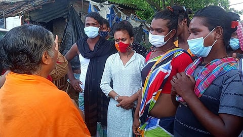 Trans women stand in masks talking to someone wearing orange.