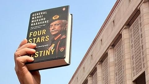 A hand holds up Naravane’s unpublished memoir, Four Stars of Destiny, in front of Parliament.