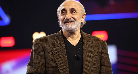 Image of Gad Saad speaking with attendees at the 2023 AmericaFest at the Phoenix Convention Center in Phoenix, Arizona. Saad is wearing a brown checked blazer and black shirt. He stands under bright lights on a stage.