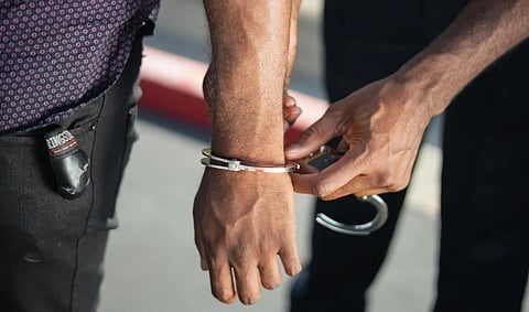 A close-up of an officer placing handcuffs on a person's wrists outdoors. The scene conveys a sense of arrest and law enforcement action.