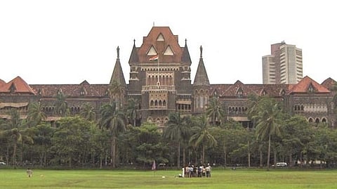 Historic building with Gothic architecture, featuring pointed arches and red rooftops, set amidst lush greenery and palm trees. A group of people gather on the lawn, conveying a serene, formal atmosphere.