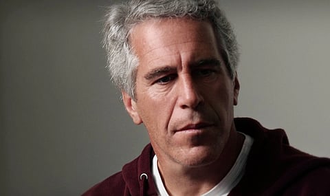 Image of convicted sex offender Jeffrey Epstein in a red jacket. the background is dim and grey.