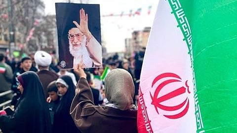 A crowd gathers outdoors, holding an Iranian flag and a poster of Iran Prime Minister. The scene conveys a sense of unity and patriotism.