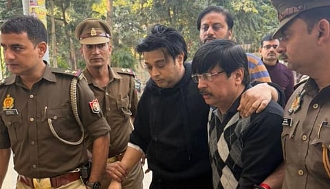 A group of police officers escort two men outdoors. The men appear serious and subdued. The officers wear uniforms, conveying a sense of authority.