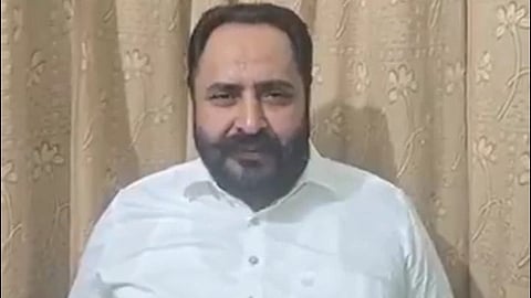 AAP MLA Harmeet Singh Pathanmajra in a white shirt sits against a beige curtain with floral patterns, conveying a calm and neutral tone.