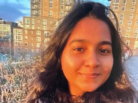 Image of  Jaahnavi Kandula 
with long dark hair in sunlight, standing outdoors. Background shows urban buildings and blue sky. 