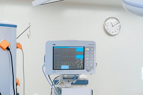 Medical monitor displaying vital signs in a hospital room. A wall clock in the background shows 10:10. The scene is calm and clinical.