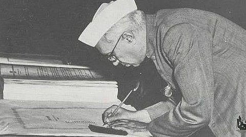 Jawaharlal Nehru is shown writing something in a paper