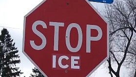 Red octagonal sign reads "STOP ICE" in bold white letters. Background has bare trees and cloudy sky, conveying a cold, winter atmosphere.
