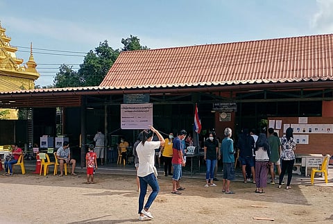 Several people stand in front of a polling station with red roof tiles during the 2020 elections.
