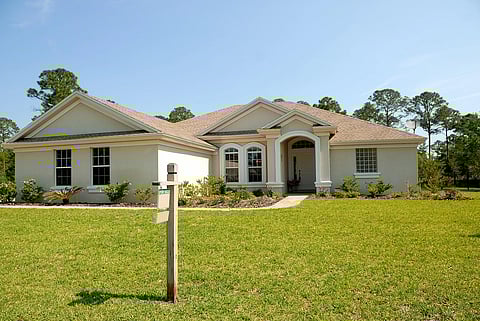 A a beige suburban house with a green lawn and a post in front.